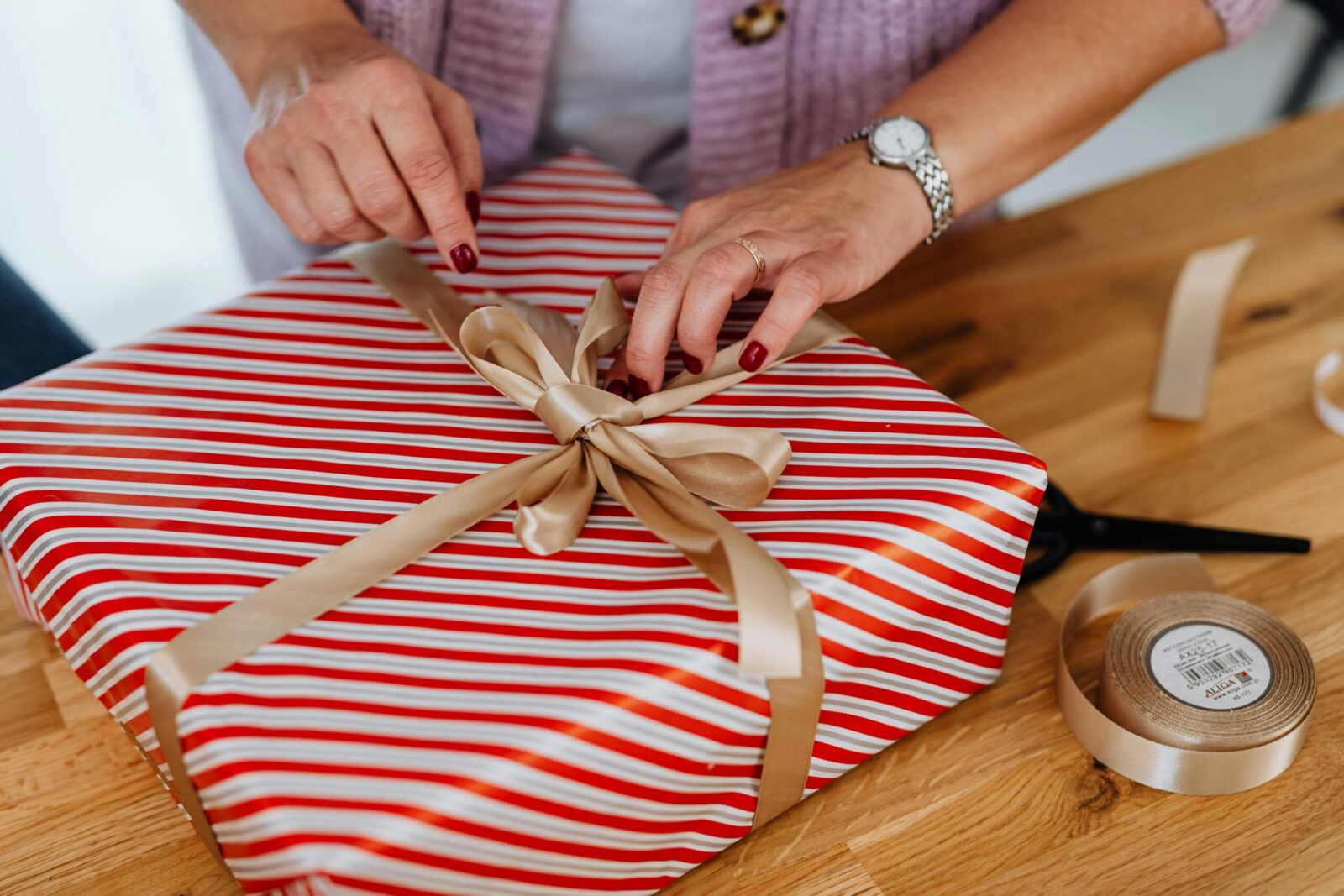 Close-up of adult wrapping a striped gift box with ribbon for Christmas celebration.